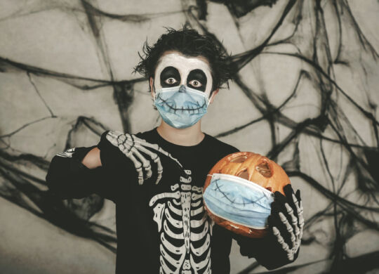 Happy Halloween,kid wearing medical mask in a skeleton costume with halloween
pumpkin	over gray background