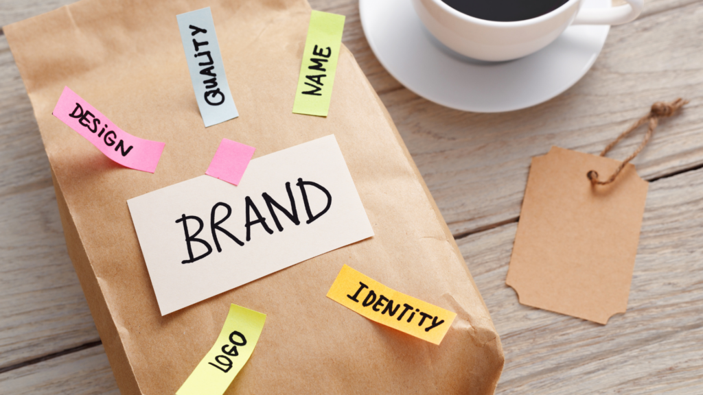 Brown package with sticky notes labeled “Brand,” “Design,” “Identity,” and “Logo,” beside blank price tag and coffee cup.