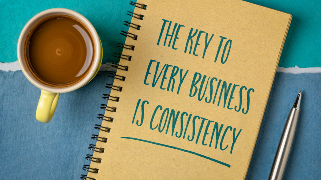 Cup of coffee, notebook, and pen on a table with the handwritten message, “The key to every business is consistency,” highlighting the importance of marketing for small business success through consistent branding and outreach.