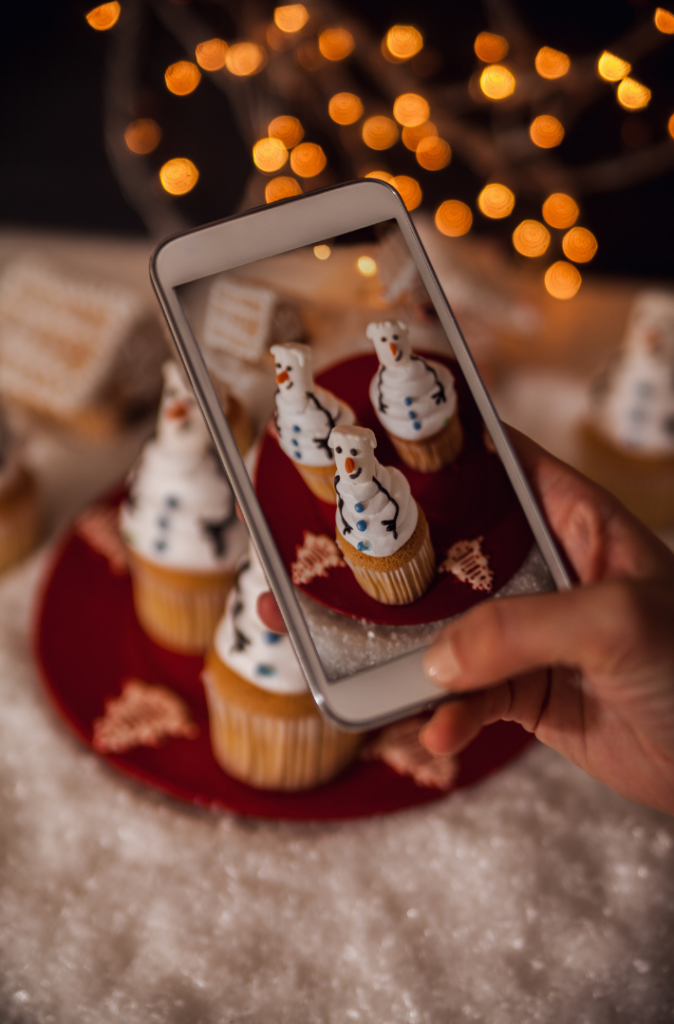 A woman's hand is taking a photo of snowman cupcakes with her iPhone.